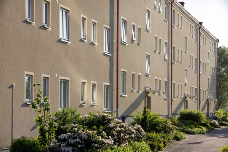 En byggnad med många fönster och buskar runt omkring.