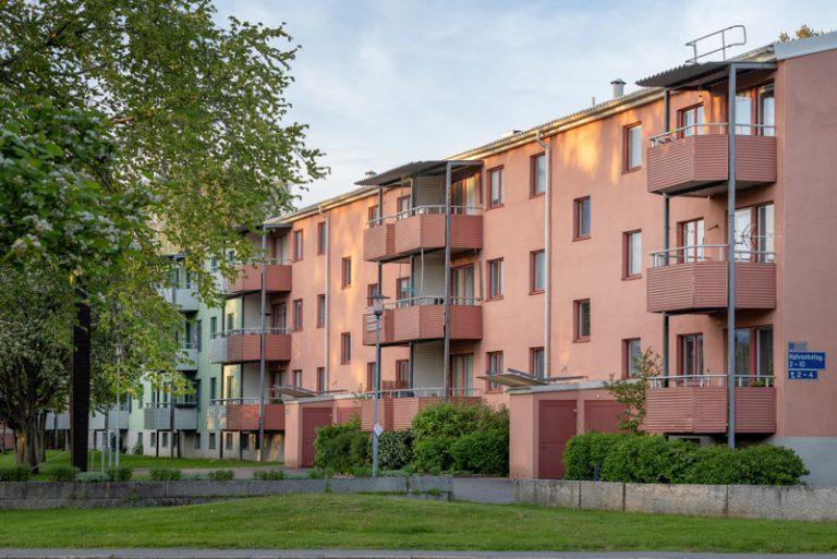 Ett flerbostadshus med balkonger, bakom gräsmatta och träd.