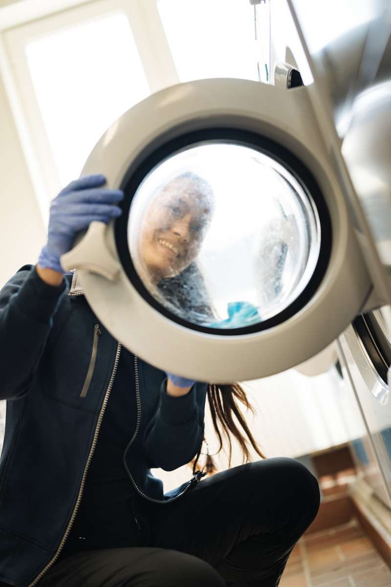 En kvinna i svart jacka tittar i en tvättmaskin. 