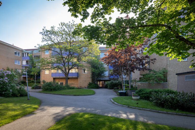 Ett hyreshus med en uppfart och träd framför sig.