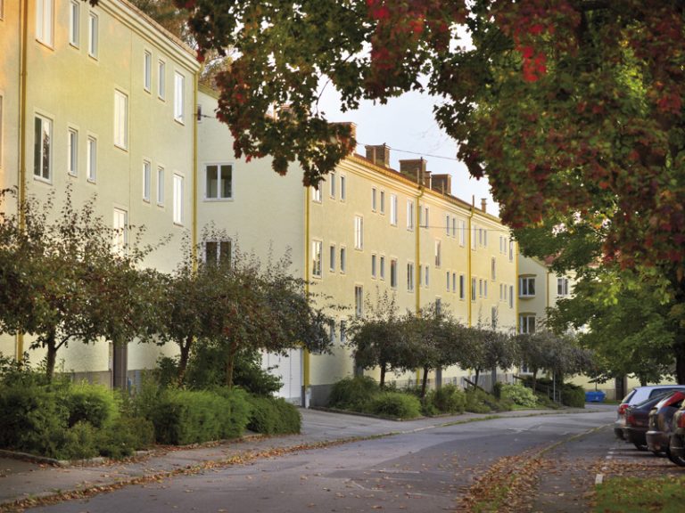 En gata kantad av parkerade bilar intill höga byggnader.