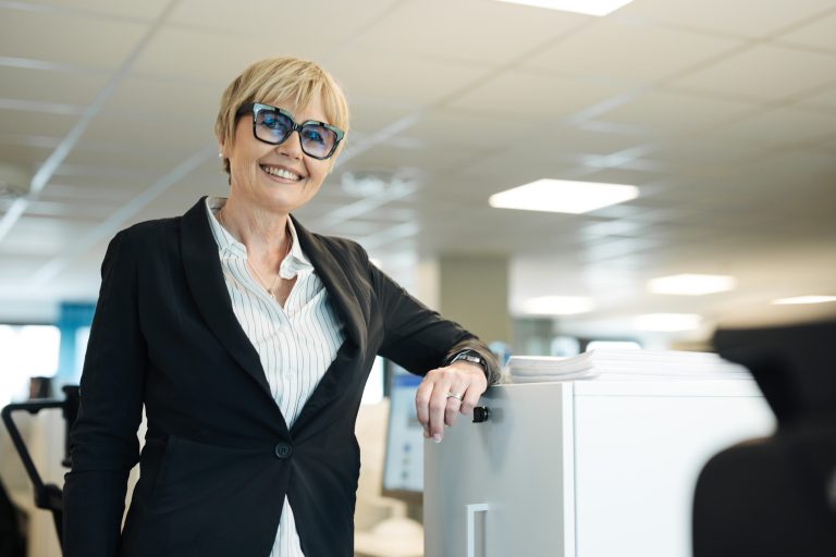 En medarbetare på Bostadsbolaget står lutad mot en dator och ler.