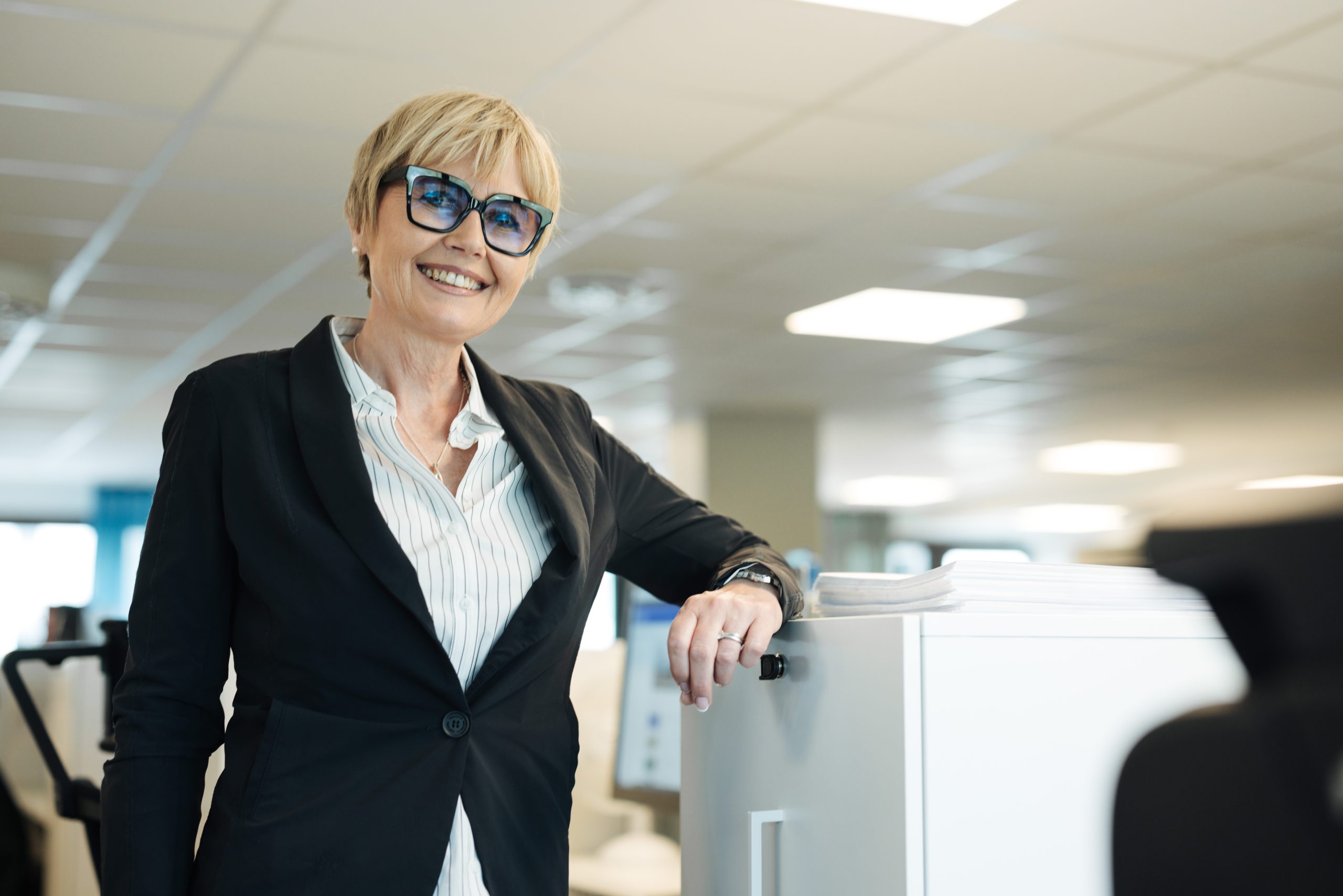 En medarbetare på Bostadsbolaget står lutad mot en dator och ler.