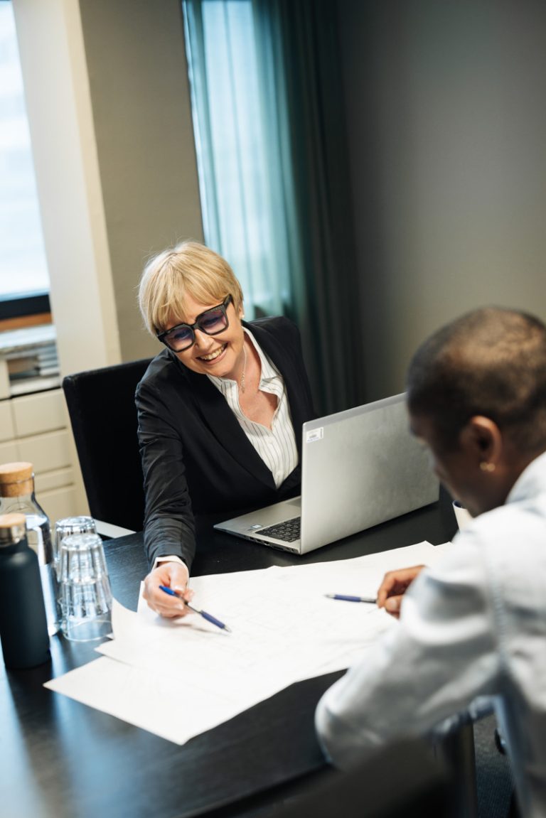 En man och en kvinna sitter vid ett bord med en bärbar dator och tittar på ett papper tillsammans.