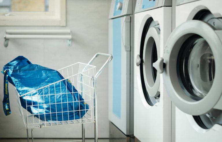 En tvättstuga med tre tvättmaskiner på rad och en tvättkorg med en påse i.