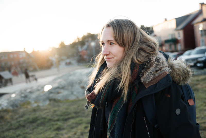 Sara, Bostadsbolagets säkerhetschef, tittar ut i fjärran. I bakgrunden syns ett bostadskvarter i kvällssol.  