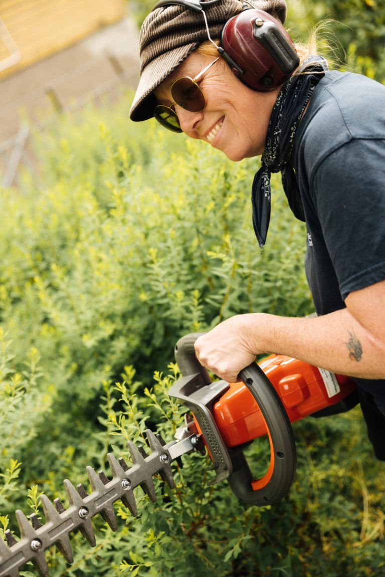 Bostadsbolagets miljövärd Pia ler och beskär en grön buske med en trimmer. 