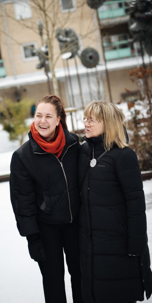 Bostadsbolagets uthyrare Jonna och Lena. De står i snön framför en beige lägenhetsbyggnad och skrattar. 