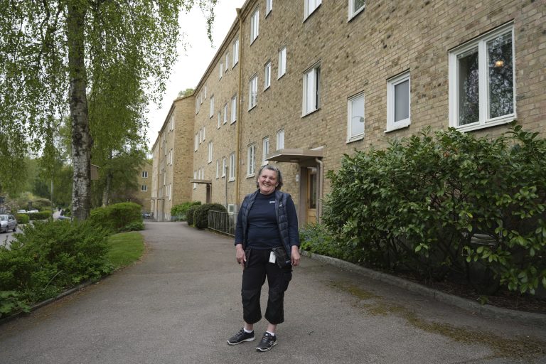 Bostadsbolagets lokalvårdare Liljana står och skrattar framför en lägenhetsbyggnad.