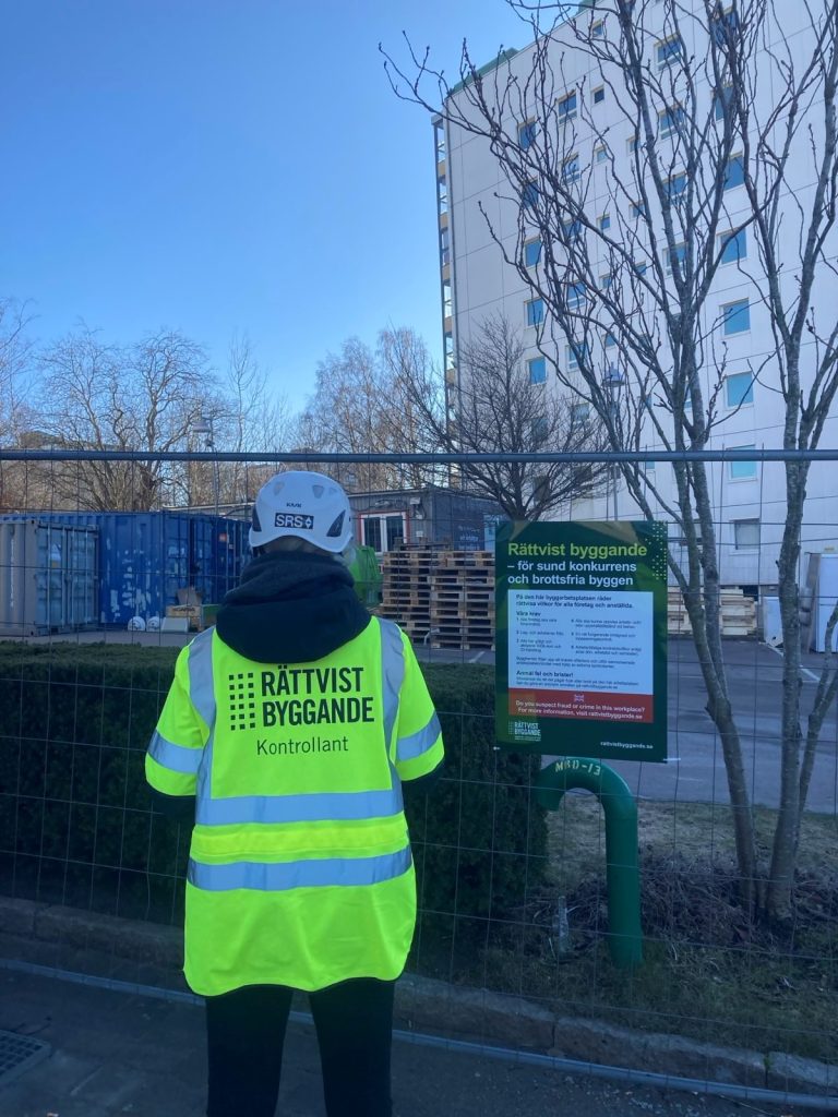 Byggarbetare bakifrån, som står framför ett stängsel. På arbetsvästen står det "Rättvist byggande".