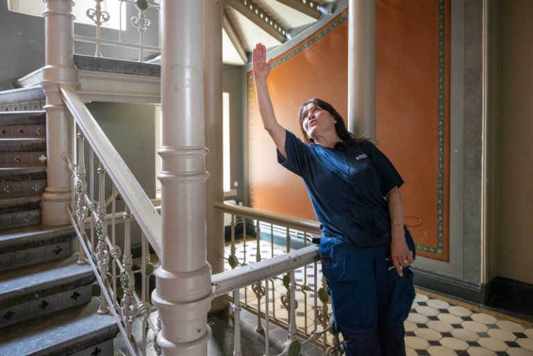 Bostadsbolagets lokalvårdare Spomenka i en trappuppgång i Vasa. Hon lutar sig mot trappräcket och pekar upp i taket. 