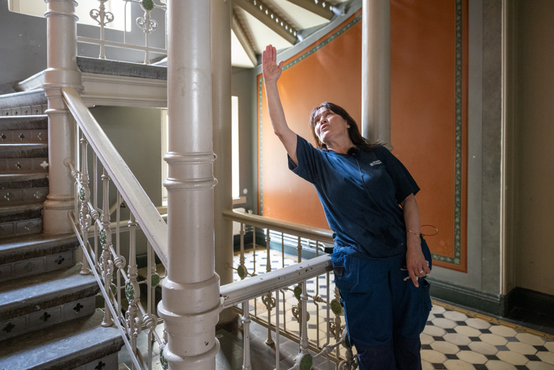 Bostadsbolagets lokalvårdare Spomenka i en trappuppgång i Vasa. Hon lutar sig mot trappräcket och pekar upp i taket. 