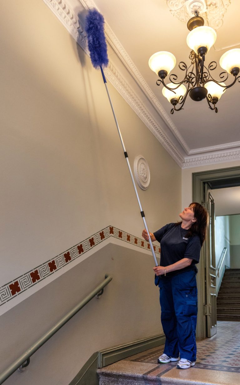 Bostadsbolagets lokalvårdare Spomenka i en trappuppgång i Vasa, som håller i en dammvippa som hon dammar taket med.