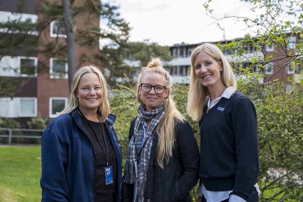 Bostadsbolagets ombyggnadssamordnare Anna, Sandra och Camilla står framför lägenhetsbyggnader på Träkilsgatan i Göteborg och ler.