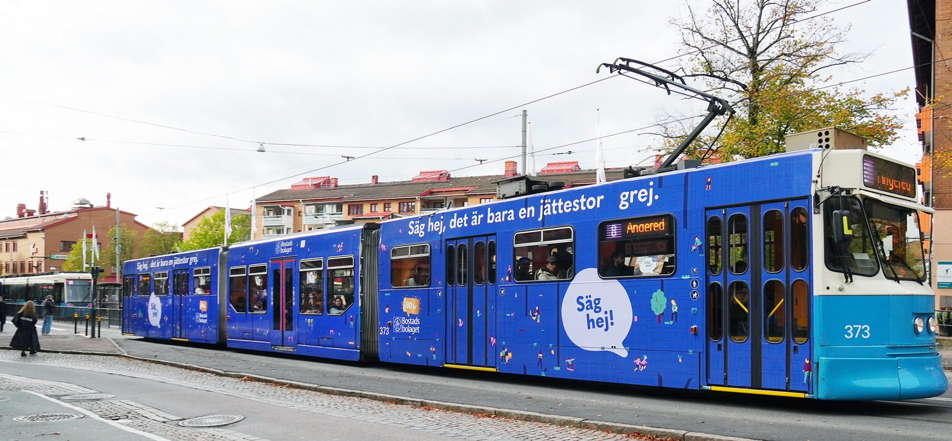 En blå och vit spårvagn markerad med Bostadsbolagets logotyp, som färdas längs en gata i Göteborg.