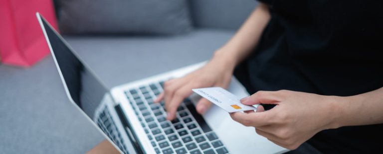 Bild på en kvinna som håller i ett betalkort. Framför henne står en dator. 