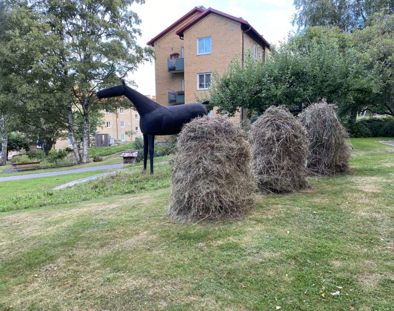 En häst som står bredvid en hög med hö.