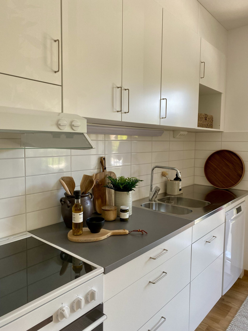 Ett kök med vita skåp och grå bänkskivor.