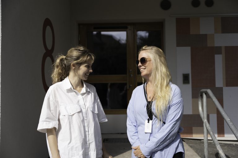 Bostadsbolagets miljösamordnare Ellen och projektledare Sandra står framför den renoverade byggnaden i Kortedala och ler i solen. 