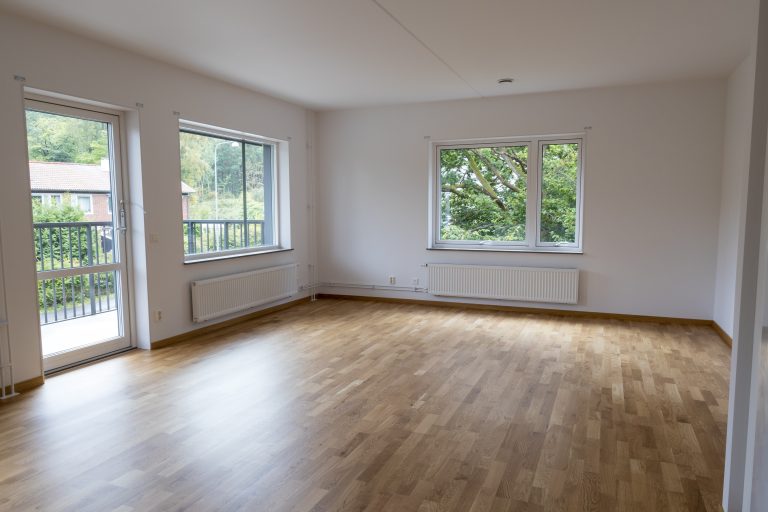 Ett tomt rum med trägolv och fönster.