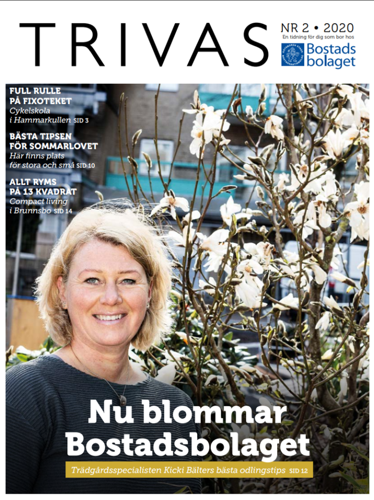 En kvinna står bredvid en buske med vita blommor.