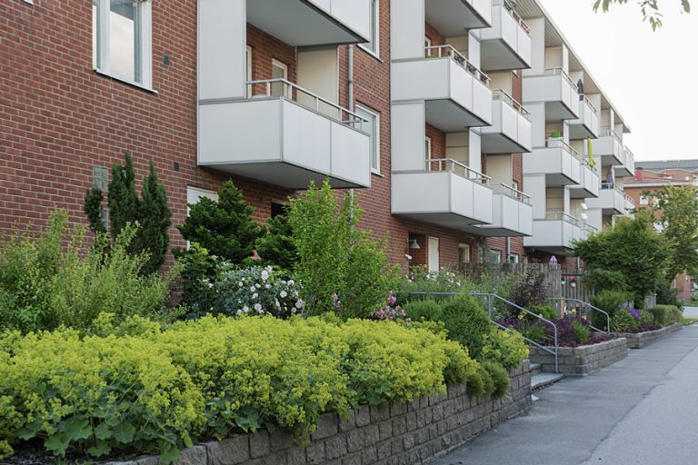 En tegelbyggnad med balkonger och buskar framför.