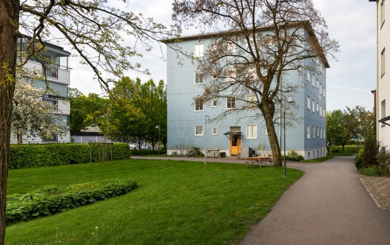 En blå byggnad som ligger intill en grönskande park.