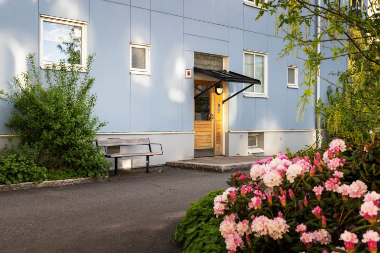 En blå byggnad med en gul dörr och en bänk framför.