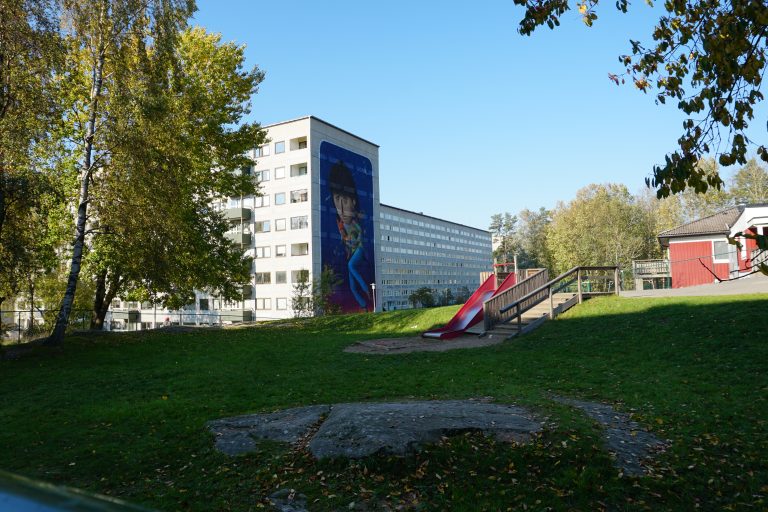 En park med en rutschkana och en byggnad i bakgrunden.