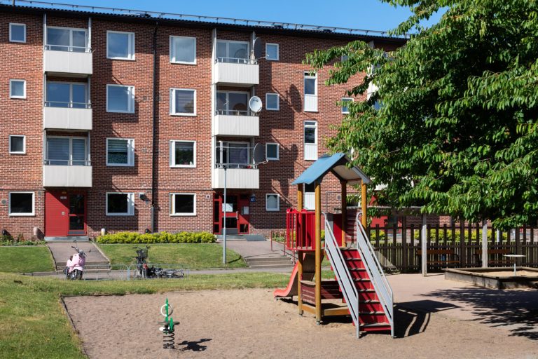 En lekplats framför ett flerfamiljshus i tegel.