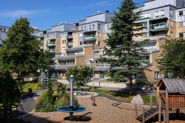 En lekplats i ett bostadsområde med träd och byggnader i bakgrunden.