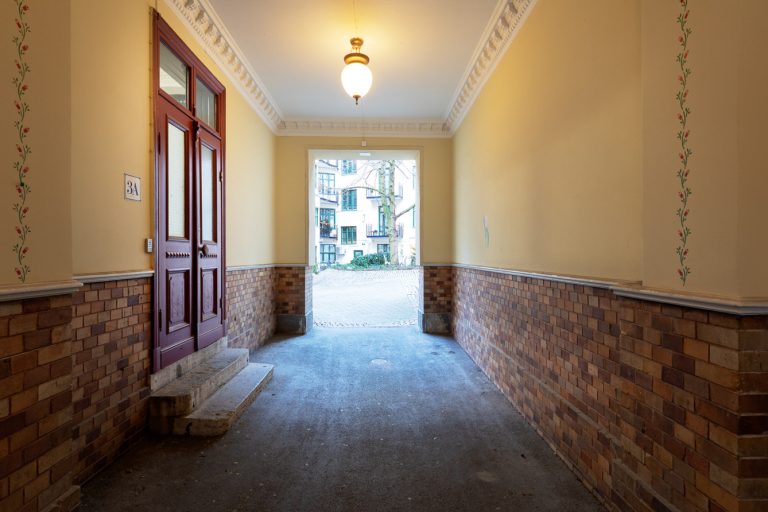 En tom korridor med en röd dörr och en tegelvägg.