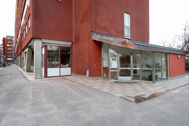 En tom asfaltsyta framför en röd byggnad.