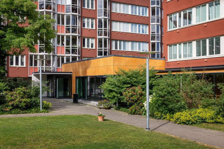 En hög byggnad med många fönster intill en park.