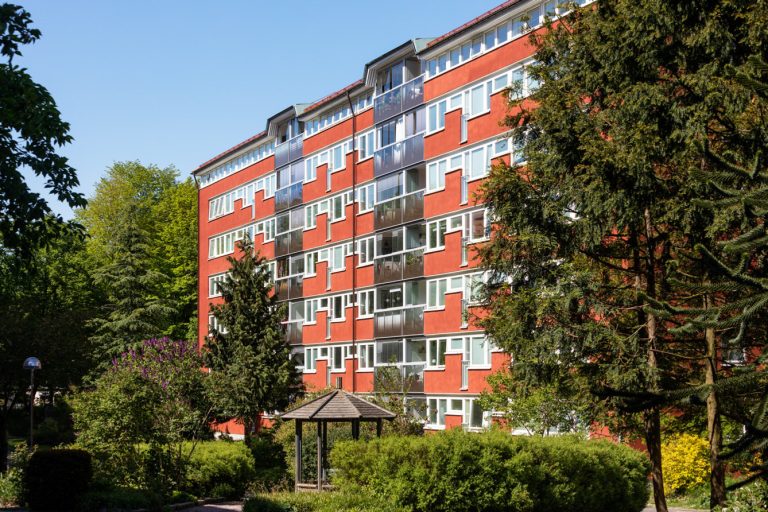 En hög röd byggnad som ligger intill en grönskande park.