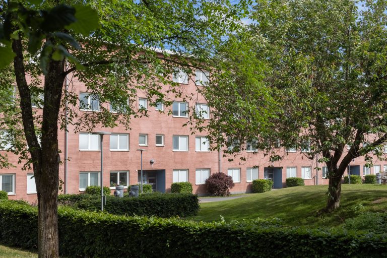 En röd tegelbyggnad omgiven av träd och gräs.