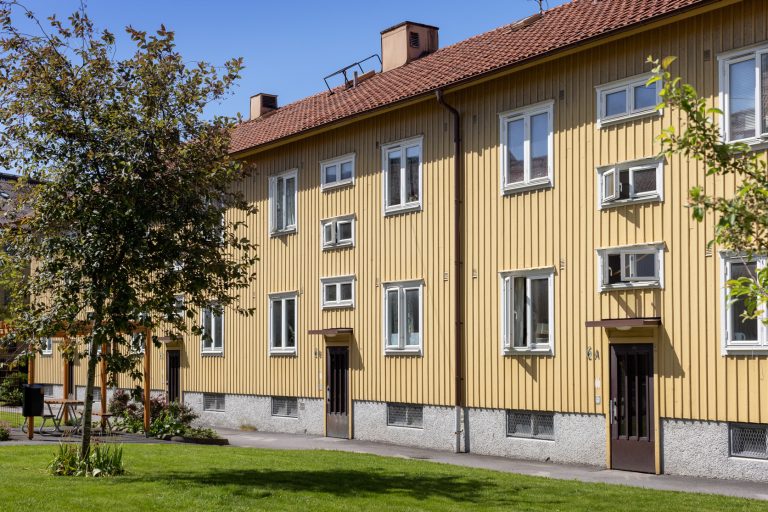 En gul byggnad med många fönster och ett träd framför den.