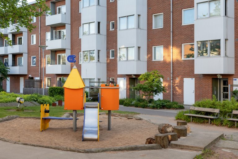 En lekplats framför ett flerfamiljshus i tegel.