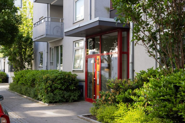 En byggnad med röd dörr och buskar framför.