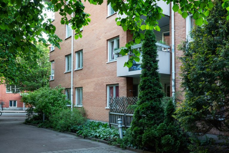 Ett hyreshus i tegel med grönskande buskar framför.