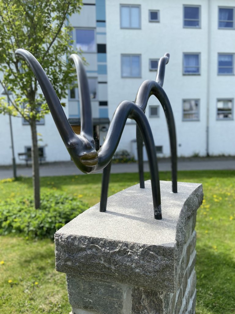 En skulptur av en spindel på ett stenblock framför en byggnad.