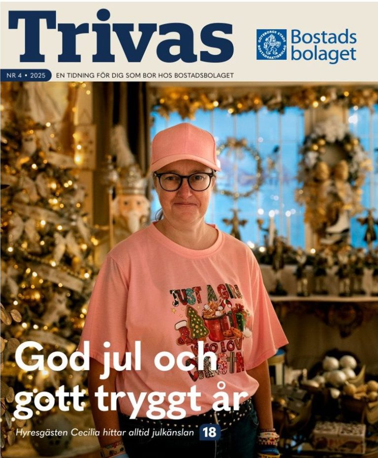 Kvinna i rosa tröja och glasögon ler in i kameran. Bakom henne syns en julgran och juldekorationer. Text i bild: "Trivas: God jul och gott tryggt år"