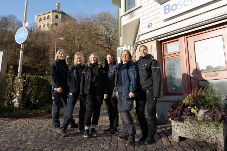 En grupp kvinnor iklädda Bostadsbolagets arbetskläder som står framför en byggnad med skylten "Boservice". 