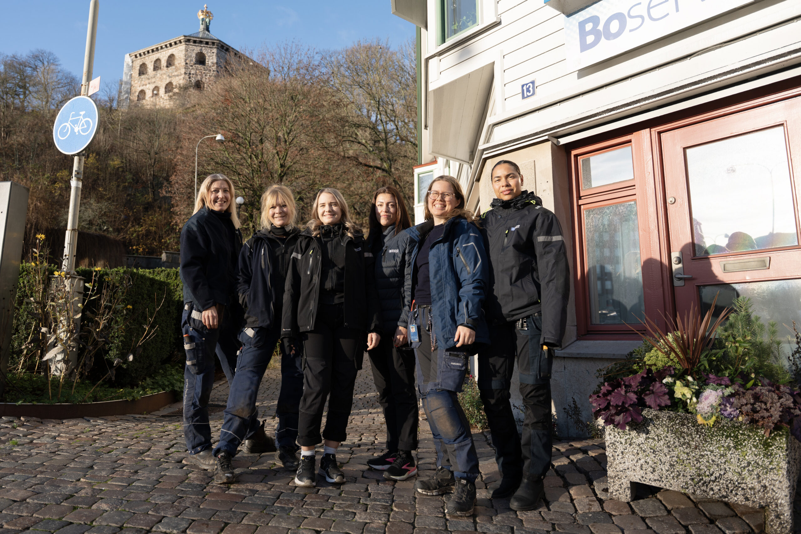 En grupp kvinnor iklädda Bostadsbolagets arbetskläder som står framför en byggnad med skylten "Boservice". 