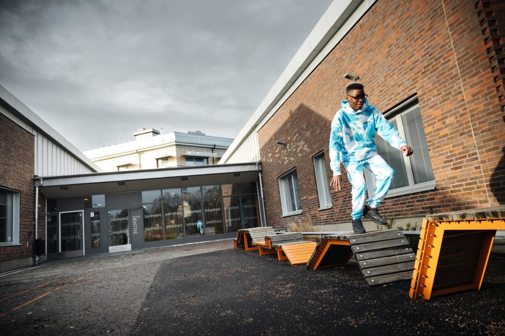 En pojke hoppar på träformationer på en skolgård.