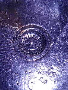 Detaljbild på avloppet i en diskho där det rinner ner vatten.