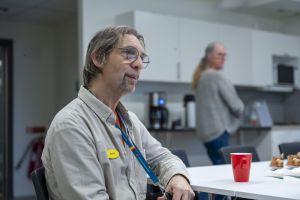 En man sitter vid ett bord med en kaffekopp. I bakgrunden syns en kvinna. 