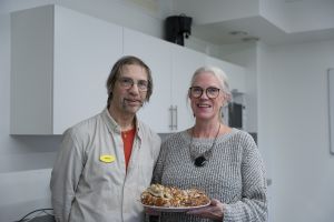 En man och en kvinna står i ett kök. Kvinnan håller et fat med bullar.