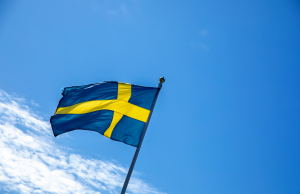 Svenska flaggan på flaggstång mot blå himmel.