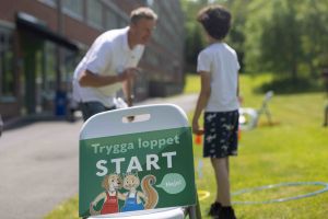 En skylt i förgrunden där det står Trygga loppet - Start. I bakgrunden syns människor.